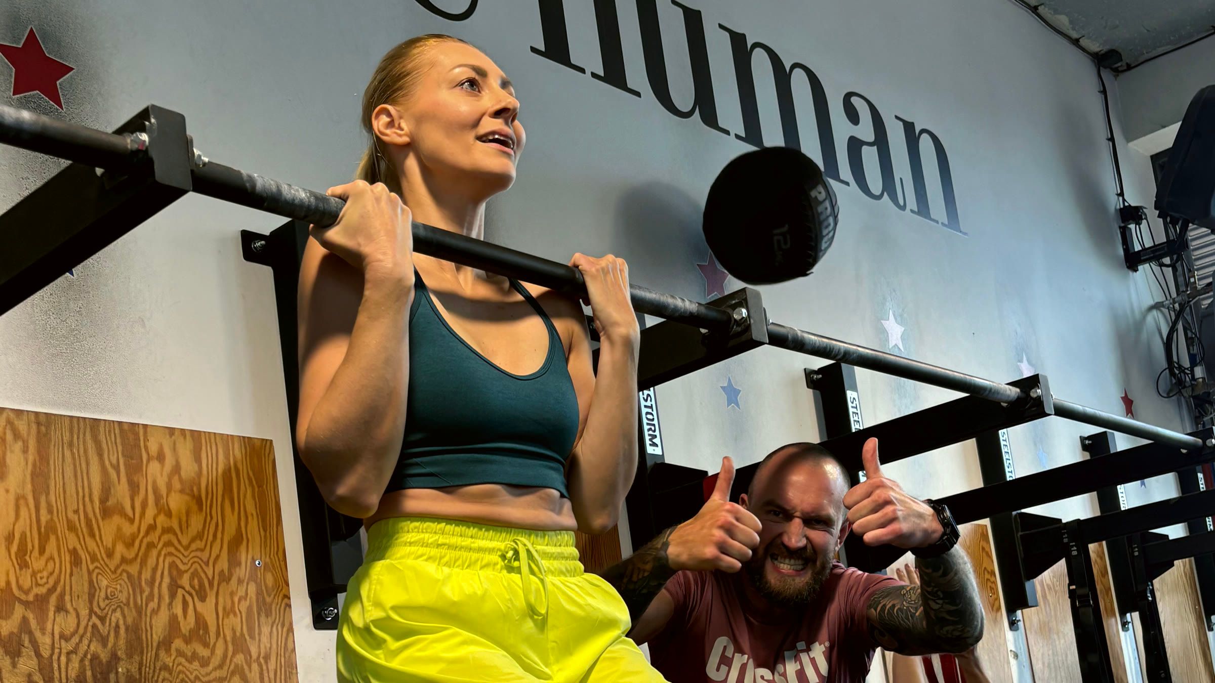 Trener pokazuje kciuki w górę osobie podciągającej się na drążku w boksie CrossFit Wilanów