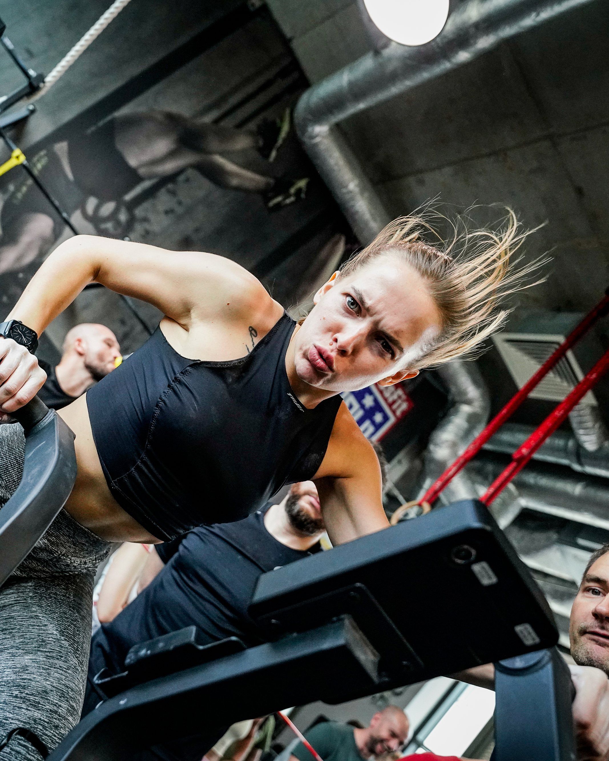 Zawodniczka w pełnym wysiłku na ergometrze w boksie CrossFit Wilanów, obserwowana przez innych
